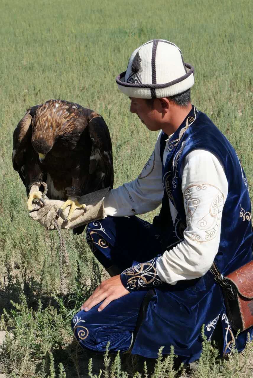 Eagle hunter in traditional Kyrgyz clothing and kalpak holding a golden eagle on a leather glove