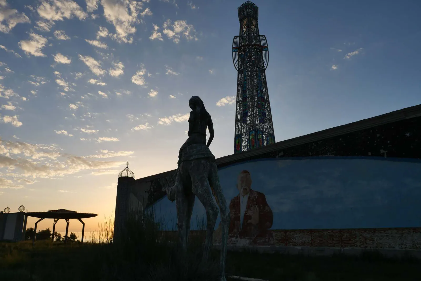 Silhouetted statue in front of a faded mural on an abandoned lakeside complex beside Issyk-Kul