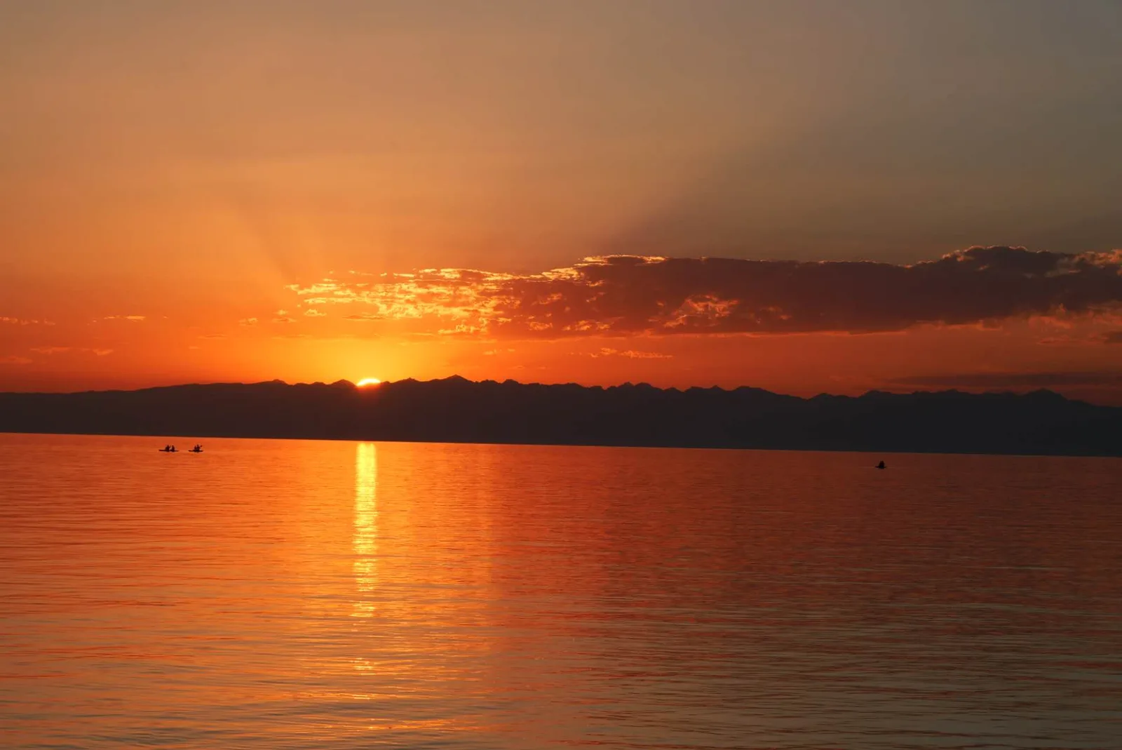 Low sun over the mountains reflected in Issyk-Kul, with small boats on the water