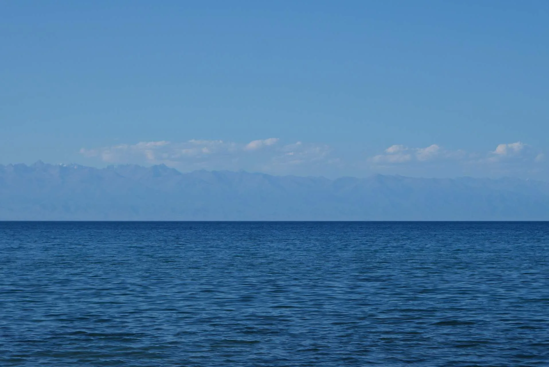 Calm blue water of Issyk-Kul stretching to a distant mountain range on the horizon