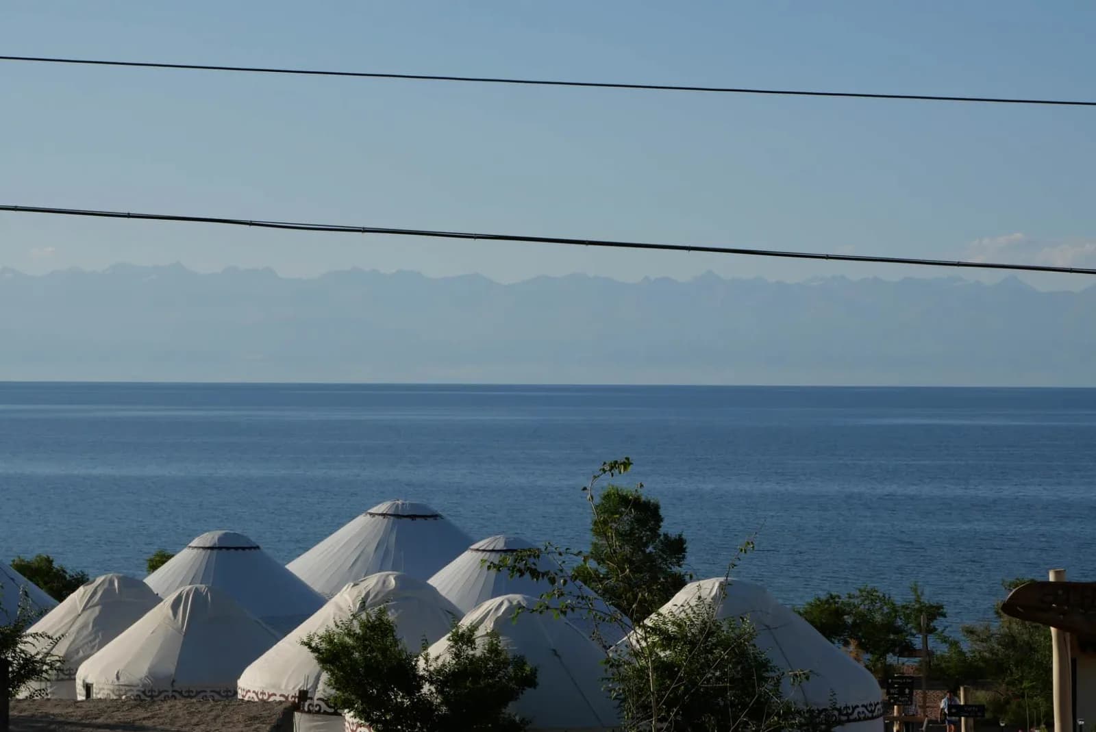 White yurts of a lakeside yurt camp overlooking Issyk-Kul, with mountains faint across the water